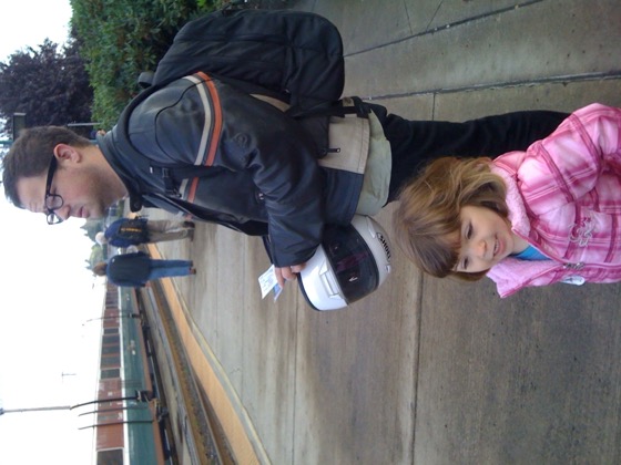 Jonathan in motorcycle gear on a train platform with his young niece Paisley in a pink jacket