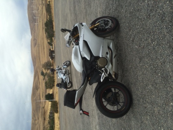 A white 2013 Ducati 1199 S at a high-desert gravel overlook with wind turbines on the hills behind