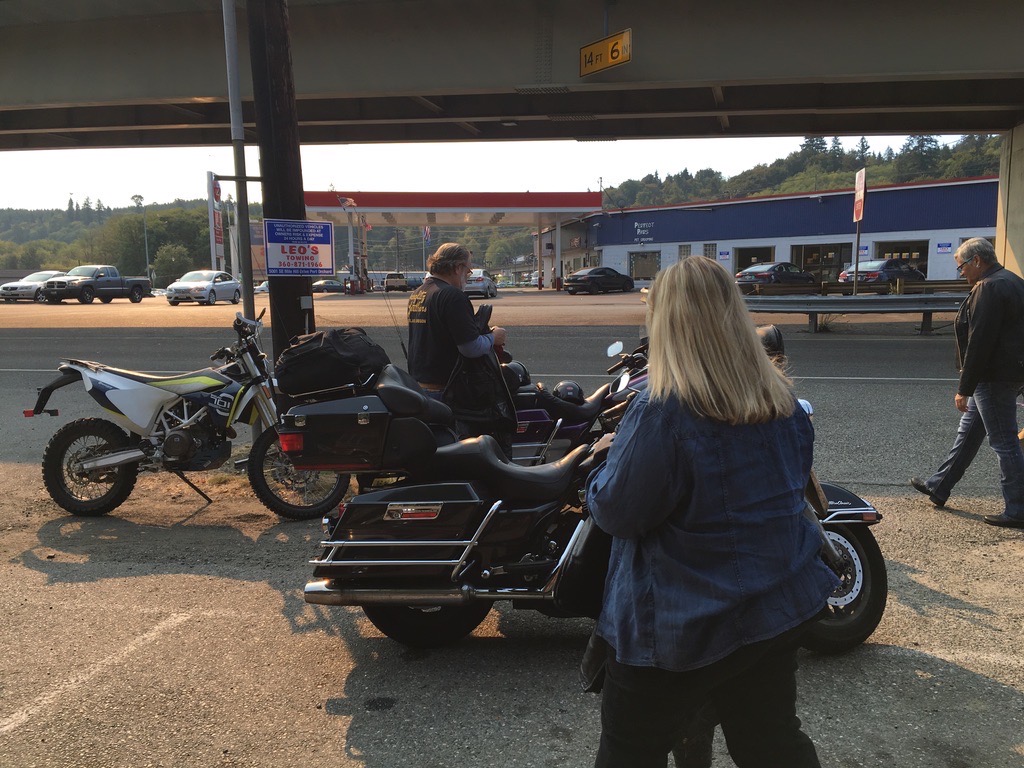 A 2016 Husqvarna 701 Enduro parked next to a Harley-Davidson bagger at a gas station with people standing around