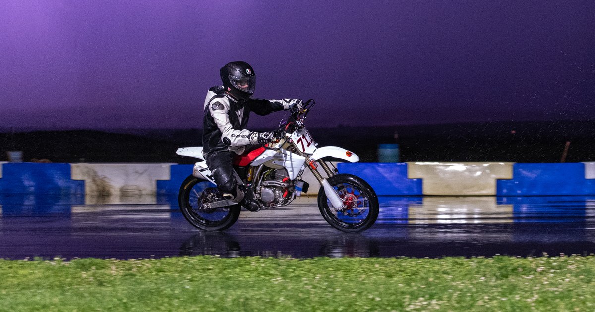 Jonathan Spiva on the Honda CRF150R #711 on a wet track under a purple storm sky at the NorthWest Mini Moto 12-Hour